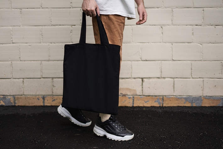 holding black cotton tote bag on a brick wall background